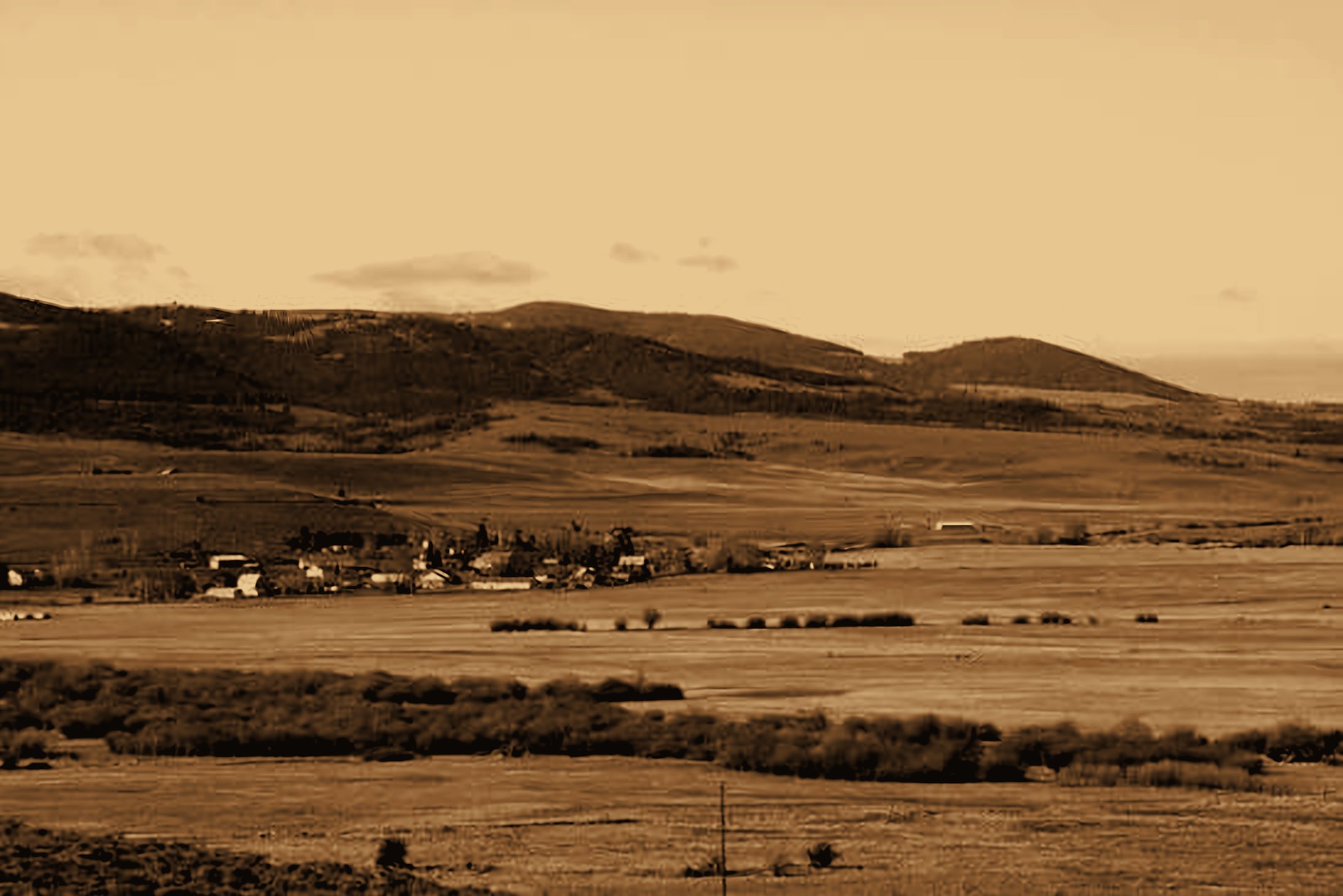 Sepia-toned photograph of a Mountain West valley town, ranch fields, and foothills
